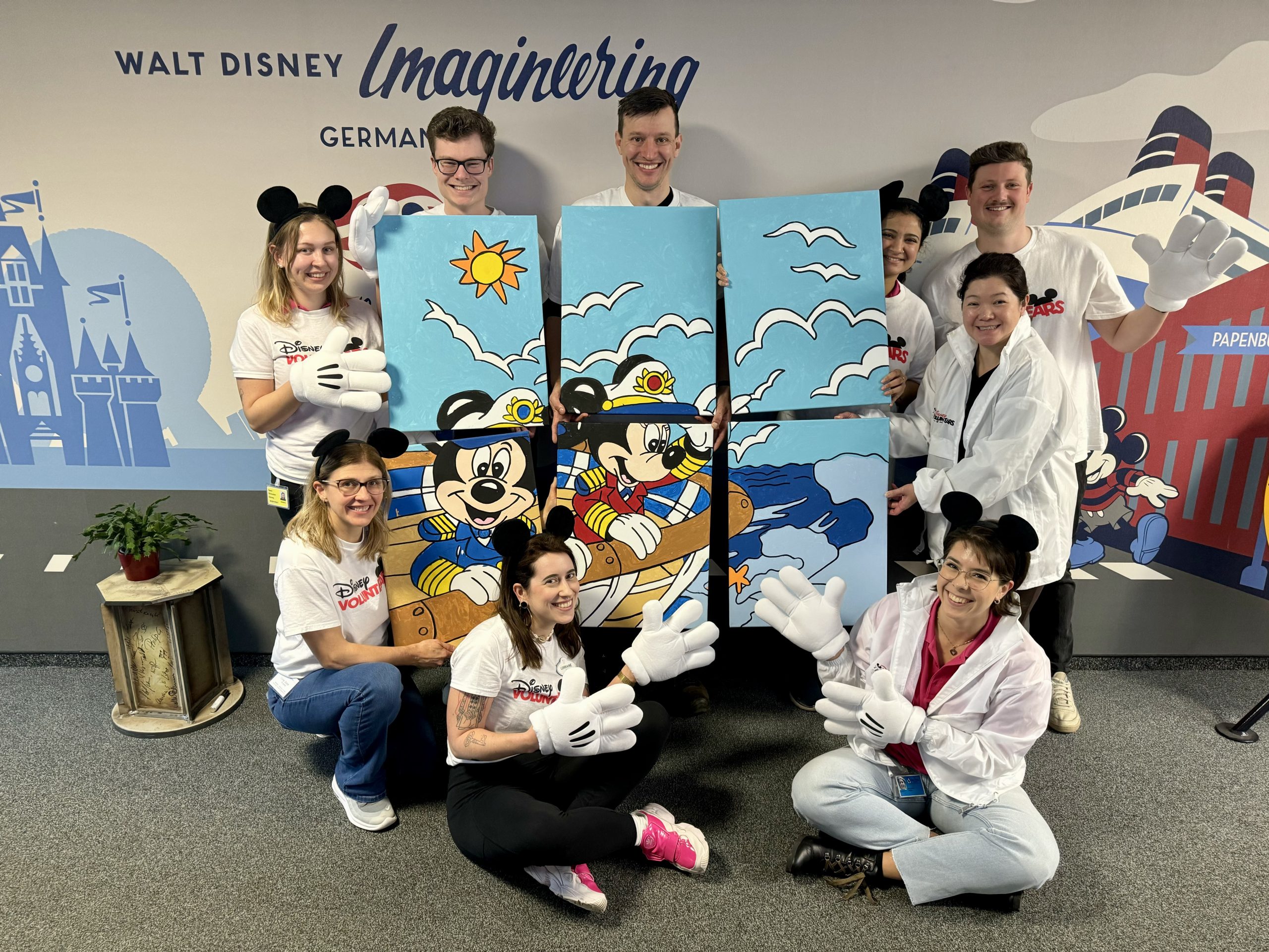 Nine Disney VoluntEARS holding six separate paintings to make one large painting of Captain Mickey and Captain Mickey.