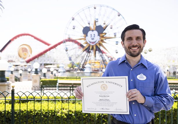 Josh holding his diploma in front of the Incredicoaster