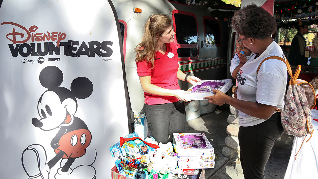 A Disney VoluntEAR Cast Member is helping another VoluntEAR at a community event.