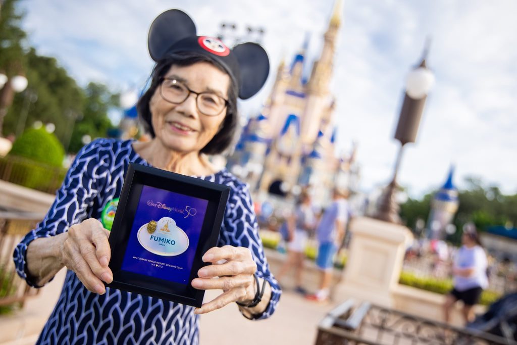 Female adult wearing Mickey Mouse ear hat and holding a shadowbox with a name tag at Magic Kingdom Park.