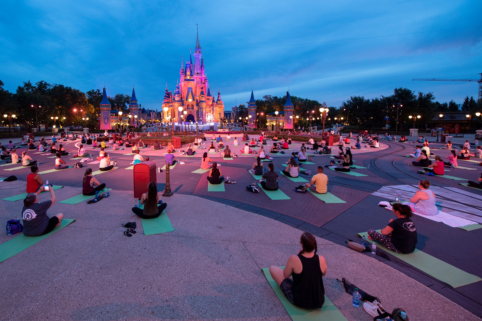 Large group of people sitting on yoga mats at sunrise inside Magic Kingdom Park.