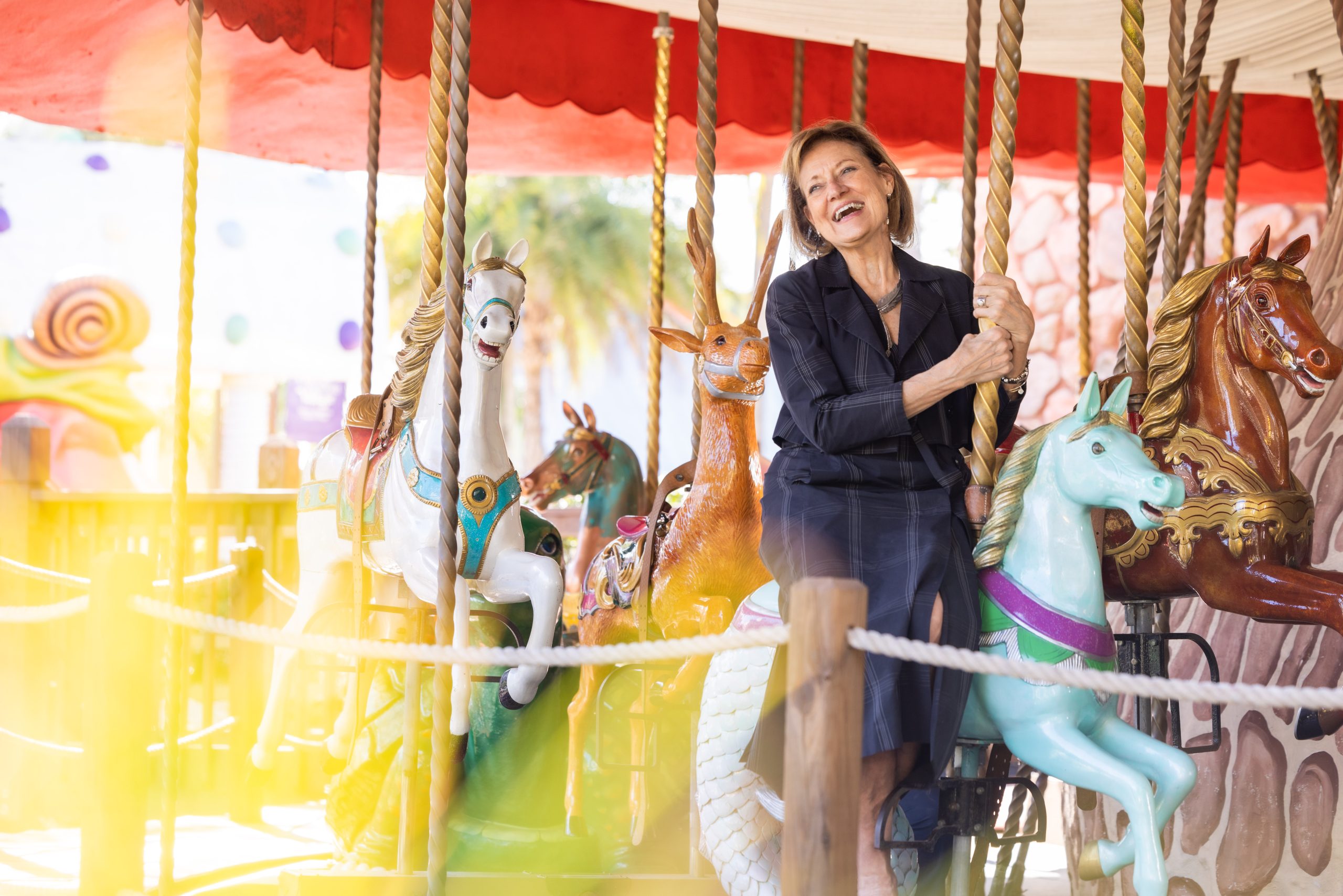 Pamela Landwirth, President and CEO of Give Kids The World Village smiles while riding a carousel.