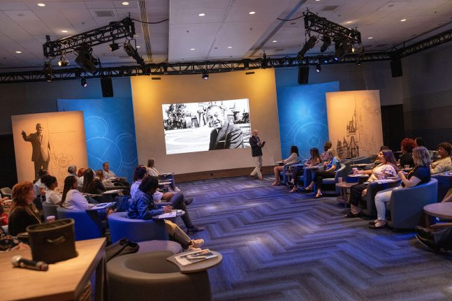 Classroom with chairs and a screen as a facilitator speaks about Disney