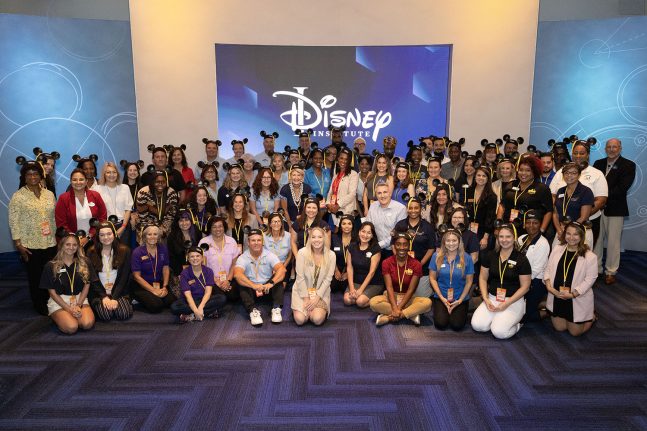 Large group of people wearing Mickey Mouse ear hats and gathered in a classroom by a screen