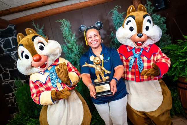 Woman holding a Mickey Mouse shaped statue and posing between Chip and Dale.