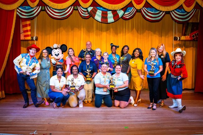 Group of People standing on stage holding Mickey Mouse-shaped awards