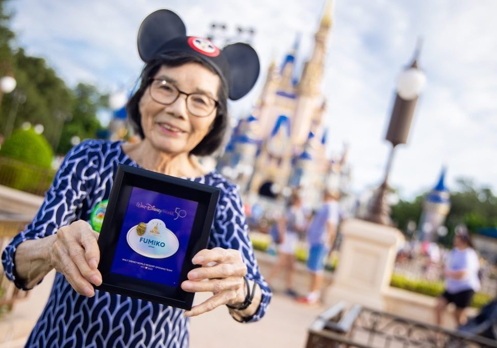 Female adult wearing Mickey Mouse ear hat and holding a shadowbox with a name tag at Magic Kingdom Park.