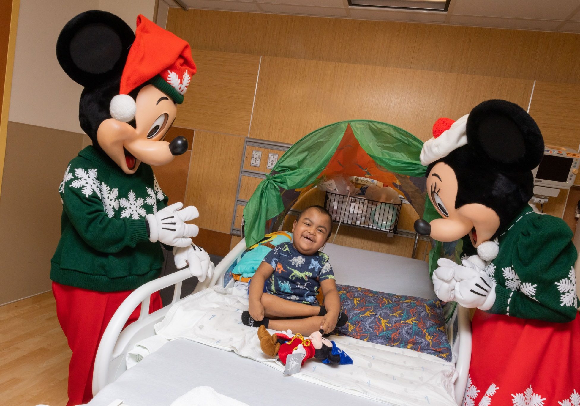 Mickey and Minnie Mouse stand over a smiling child in a hospital bed