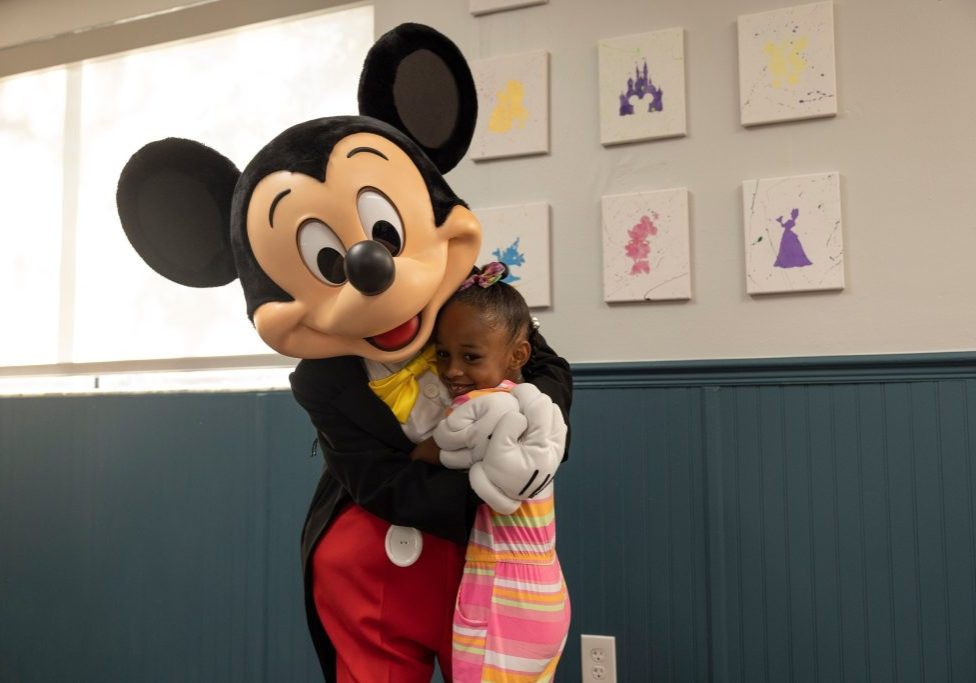 Mickey Mouse stands in the newly renovated youth center hugging a child