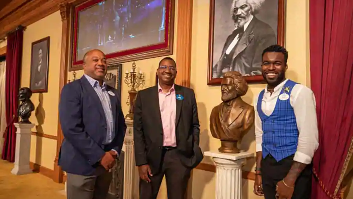 Three Cast Members pose in the Lincoln Theater, featuring a new installation honoring slavery abolitionist leader Frederick Douglass.
