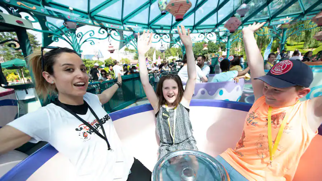 A Disney VoluntEAR rides the Mad Tea Party with two wish children.