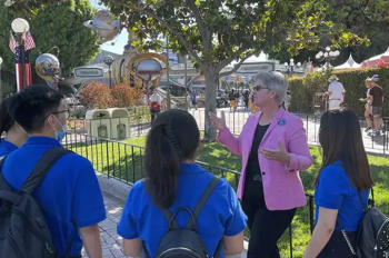 Disneyland Cast Member and Mentor is wearing a pink blazer talking to three students in royal blue tshirts.