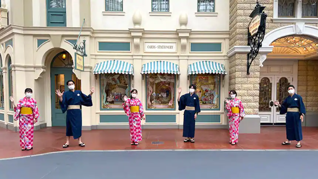 Six Cast Member stand on Main Street at Tokyo Disneyland wearing Kimonos and waving.