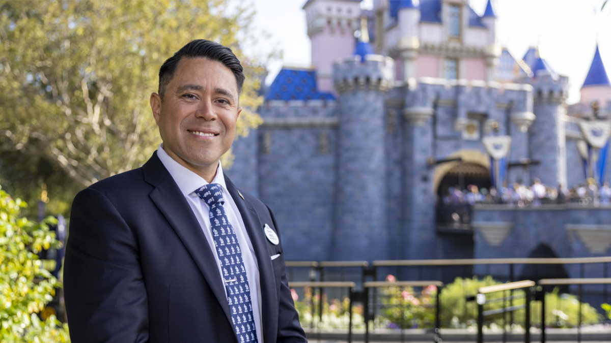 Ariel wearing a suit standing in front of Sleeping Beauty Castle at Disneyland.