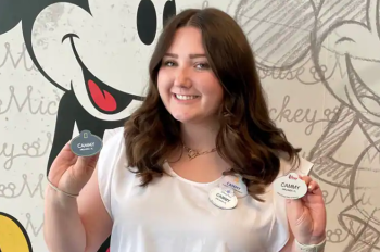 Woman with brown hair, wearing a white shirt is holding up her 4 Disney nametags in front of a Mickey sketch background.