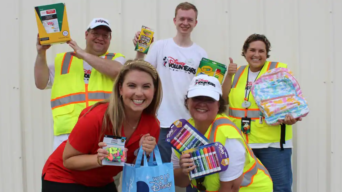 Four Cast Members in VoluntEARS T-shirts join WDW Ambassador Ali Manion in collecting Back to School supplies and posing for a photo.