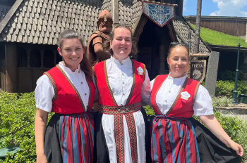 Three female cultural representatives from Norway pose for a picture together in front of the Norway Pavilion.