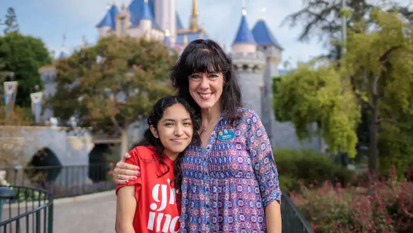 Mentoree April in a red shirt with Mentor Theresa in front of Sleeping Beauty Castle. 