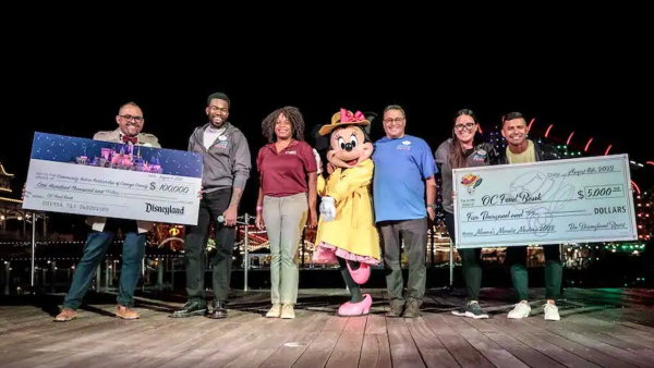 Minnie Mouse on Stage with the Disneyland Ambassadors holding two checks. 