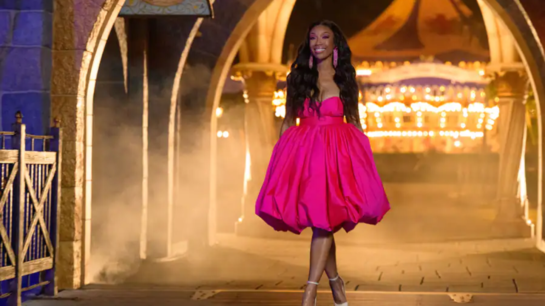 Global superstar and Grammy Award-winning recording artist Brandy walking through the archway of Sleeping Beauty Castle in a pink dress at night.