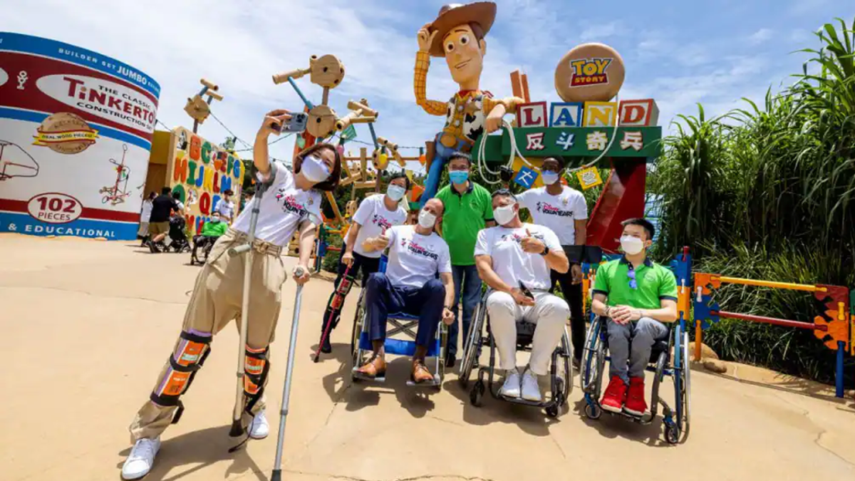 Cast Members in wheelchairs pose for a photo in Toy Story Land wearing Disney VoluntEARS shirts.