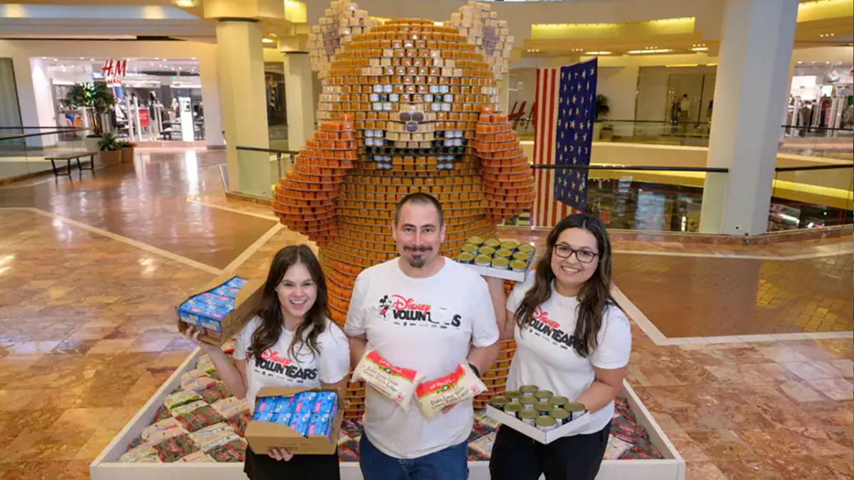 Three Cast Members pose with food donations in front of the CANda Panda.