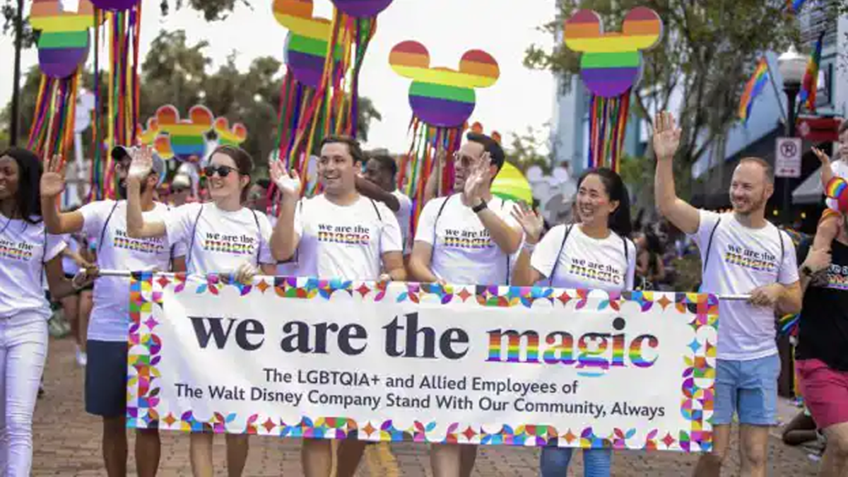 Cast Members waving in the Pride parade carrying a "We are the Magic" banner.