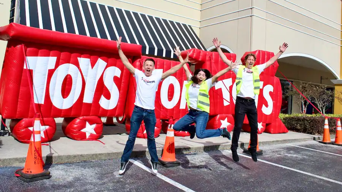 Cast Members celebrating in front of Toys for Tots blow up sign.