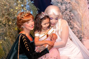 Disney Princesses Elsa and Anna embrace a little girl at Disney's Once Upon A Wish Party