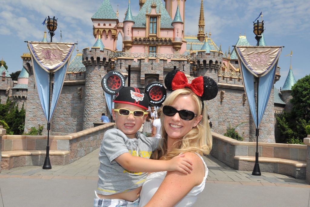 Jennifer and her son in mouse ears posing for a photo in front of Sleeping Beauty Castle at Disneyland Park.