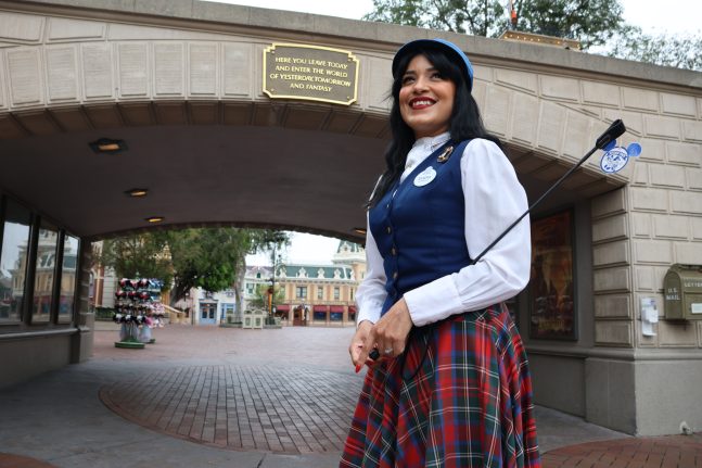 Guest Relations Core Lead and Trainer Sandra Aguirre smiles in front of the Disneyland park entrance plaque.